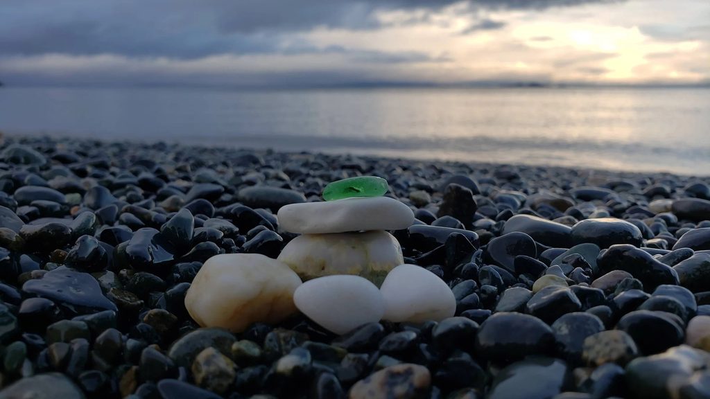 moody winter light over the ocean with a tiny single green seaglass shard perched on white beach pebbles.